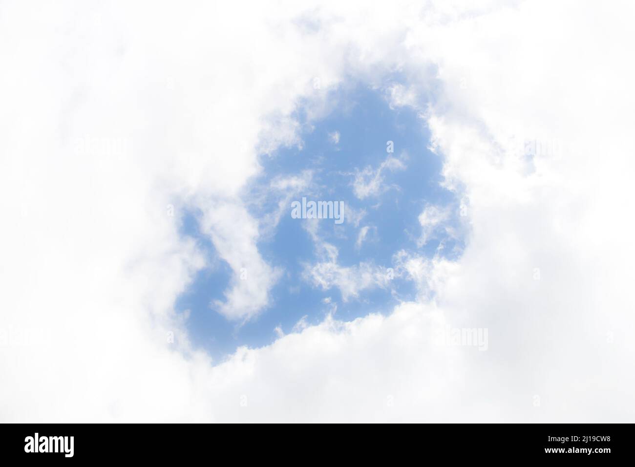 Blue sky through the eye of glowing white fluffy clouds. Stock Photo