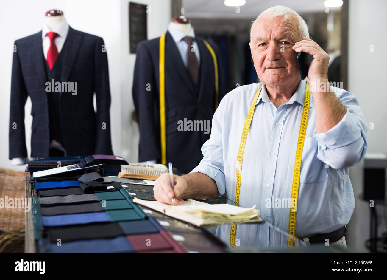 Professional tailor man talking on mobile phone and making notes in notebook Stock Photo