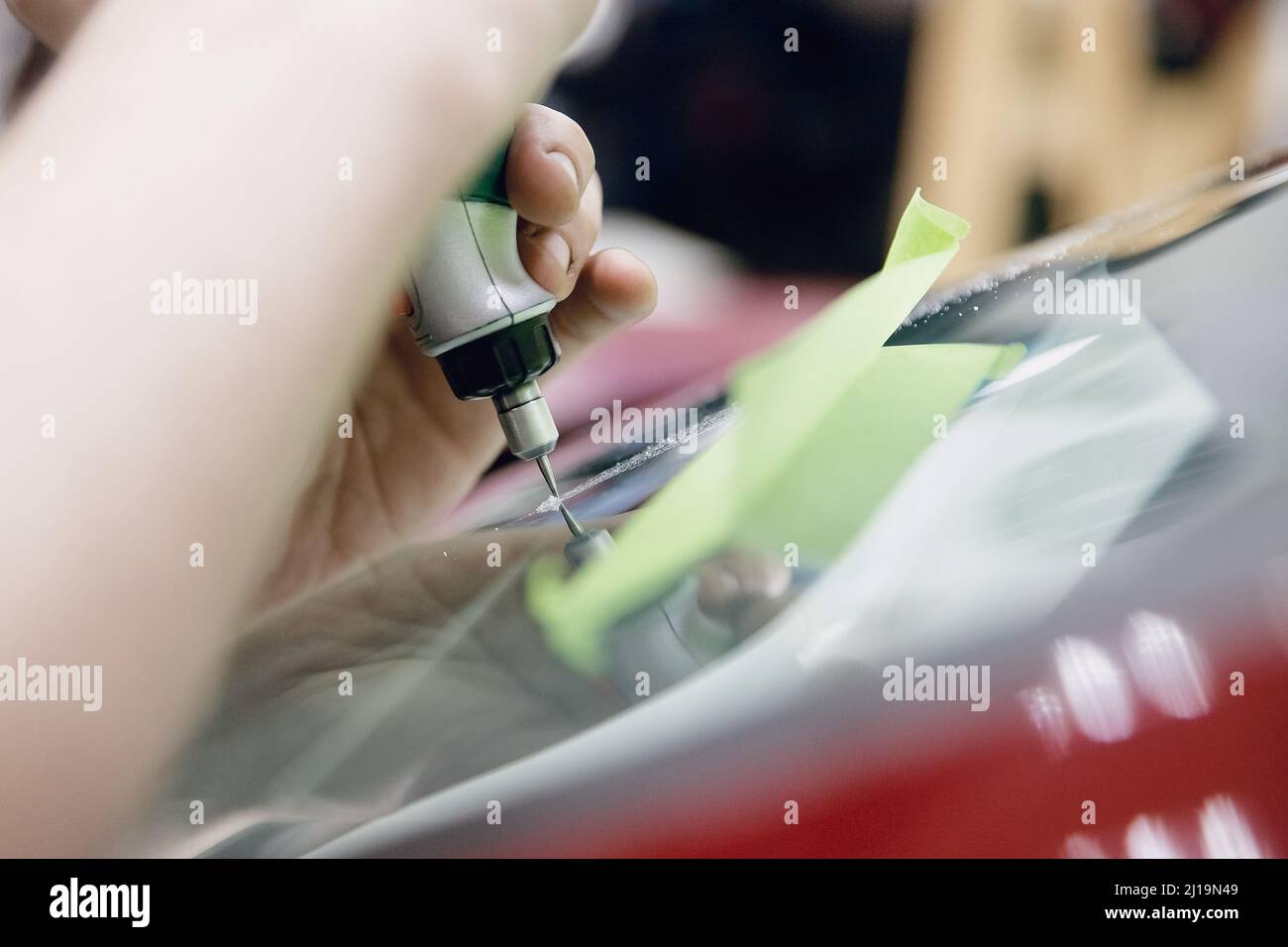 Worker fixes crack in car glass windshield, repair drills and pours
