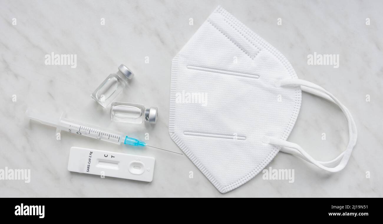 Medical mask, antigen test, vaccine bottles and syringe used for prevention and treatment during Coronavirus Covid 19 pandemic Stock Photo