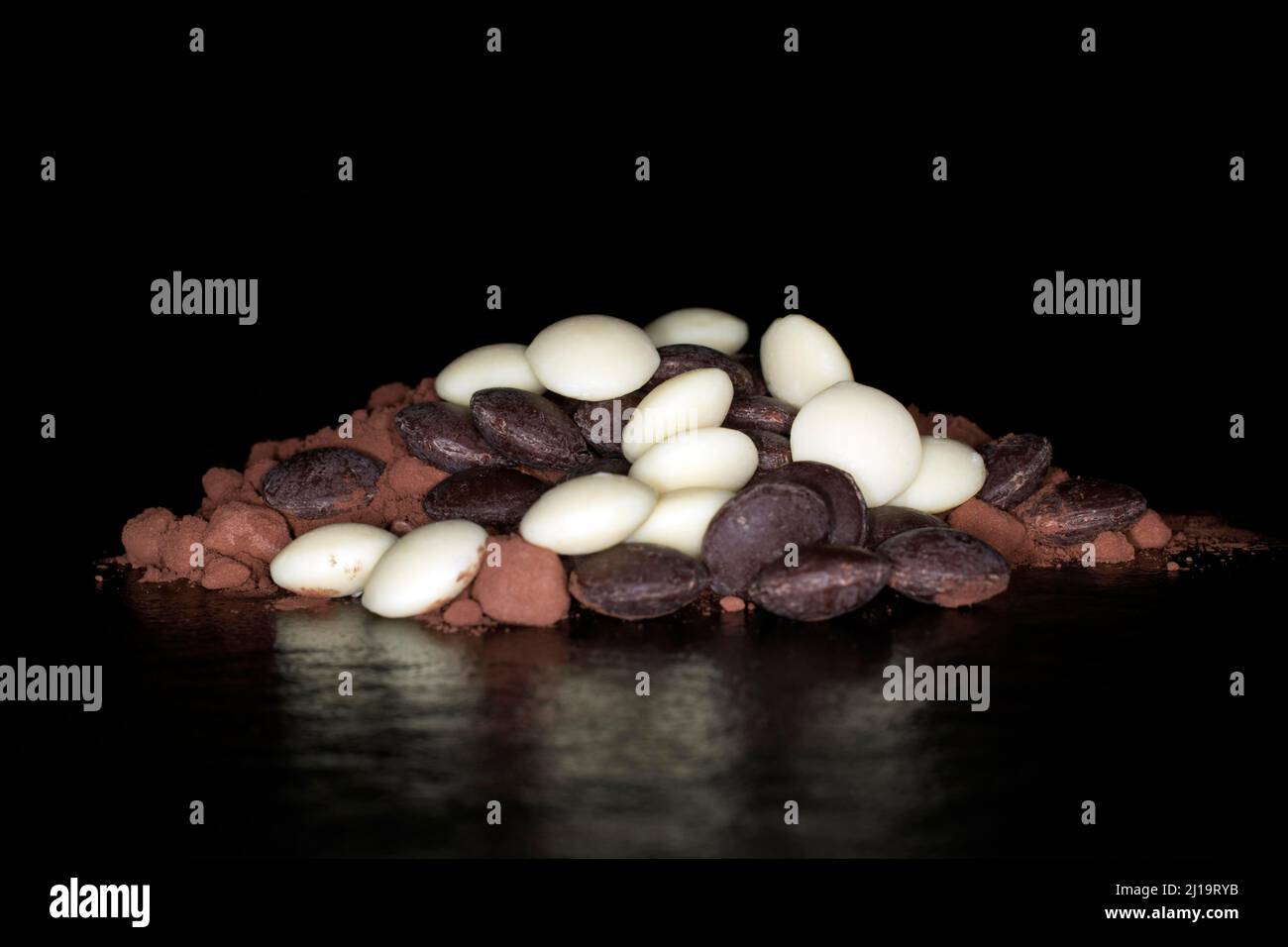 Dark and white couverture chocolate drops lying on cocoa powder, studio photography with black background Stock Photo