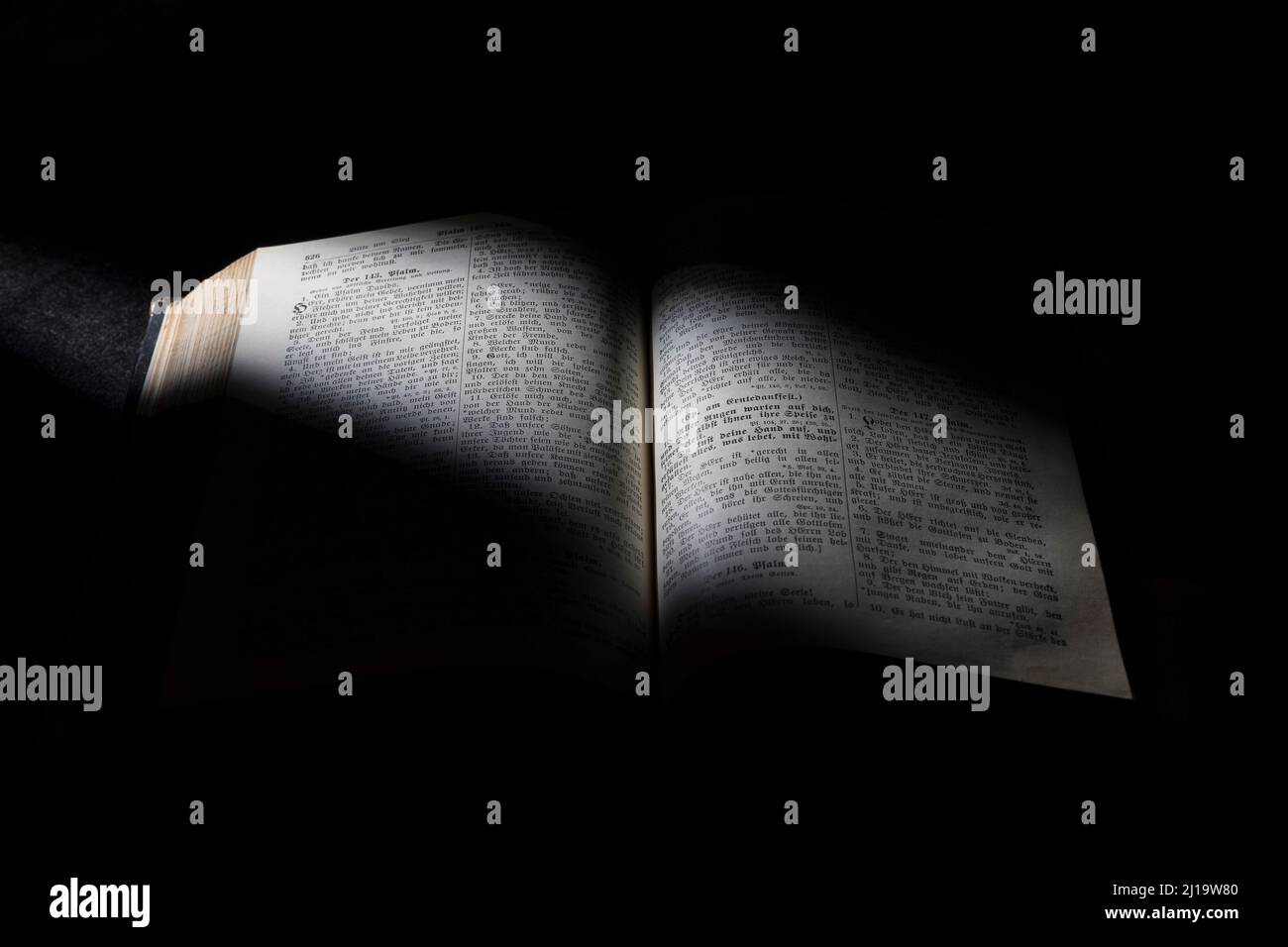 Old Bible, open book on black background, grazing light Stock Photo