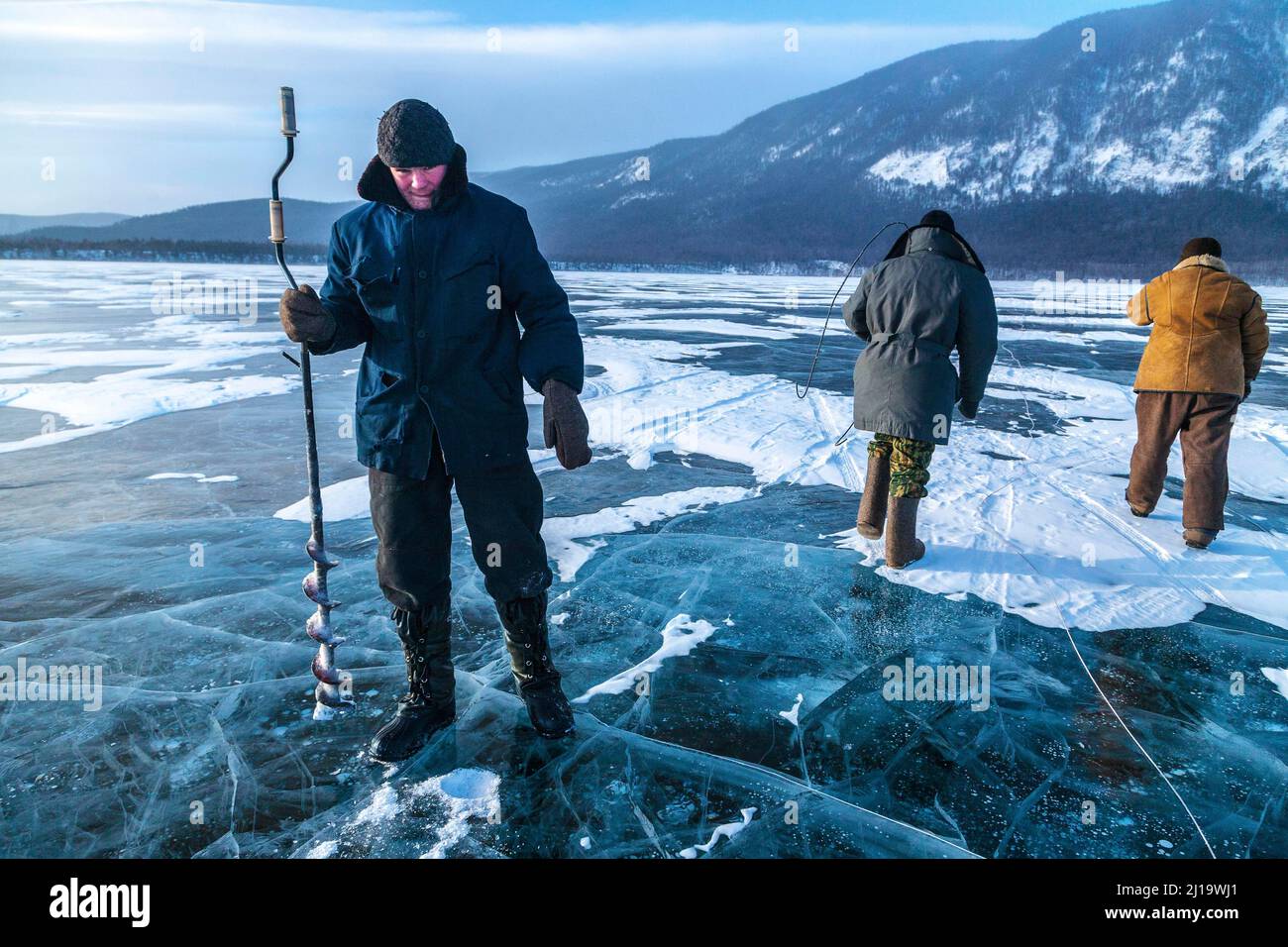 Ice fishing, A young fisherman digging a hole in the ice formed over Lake Baikal to fish, Lake Baikal, Severo Baikalsk, Siberia, Russia, Asia Stock Photo