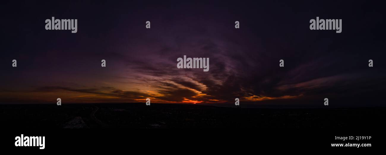 Dark wispy clouds in a deep purple sky in the afterglow of an orange sunset aerial panoramic Stock Photo