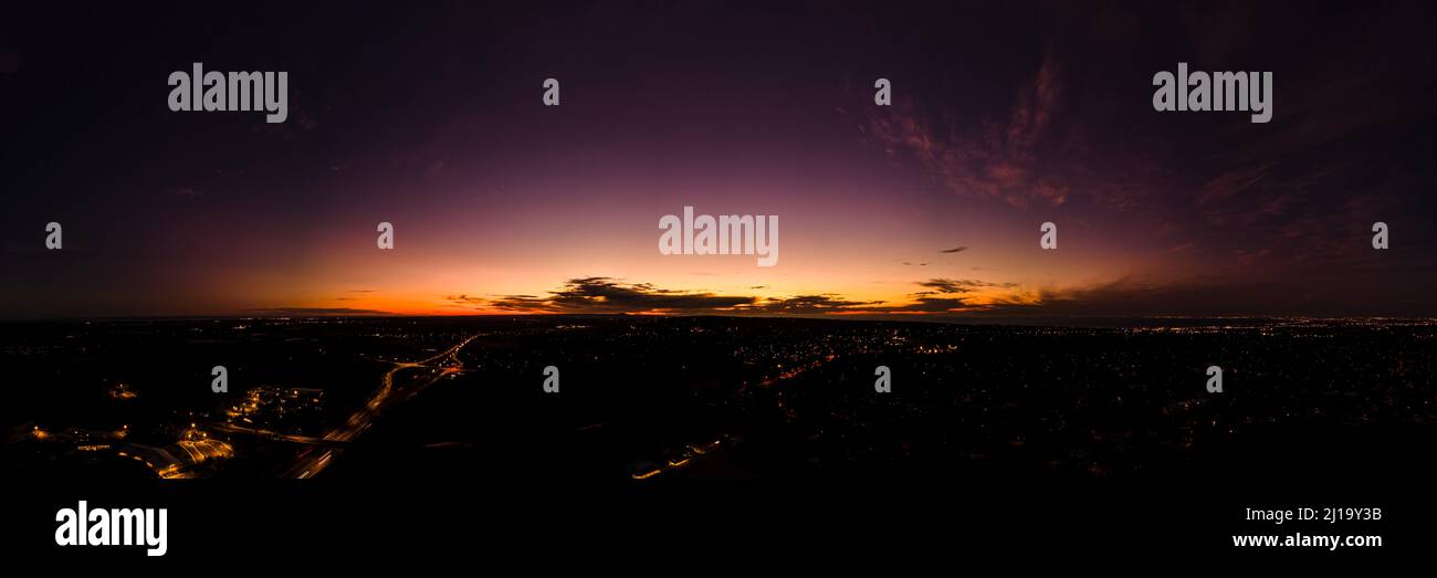 Dark horizon clouds in a deep purple sky in the afterglow of an golden sunset above the street lights aerial panoramic Stock Photo