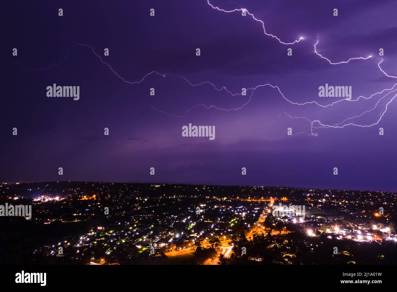 Lightning bolt discharging in the stormy clouds above the street lights aerial nighttime shot Stock Photo