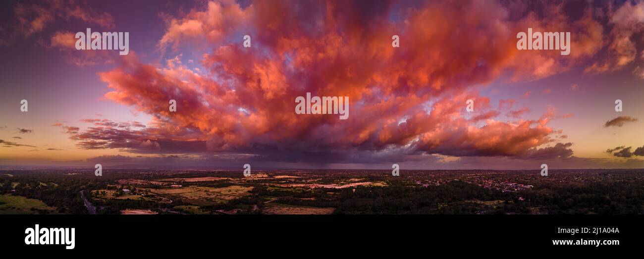 Firey storm clouds orange pink and red at sunset with distant rain storm across the landscape aerial panoramic Stock Photo