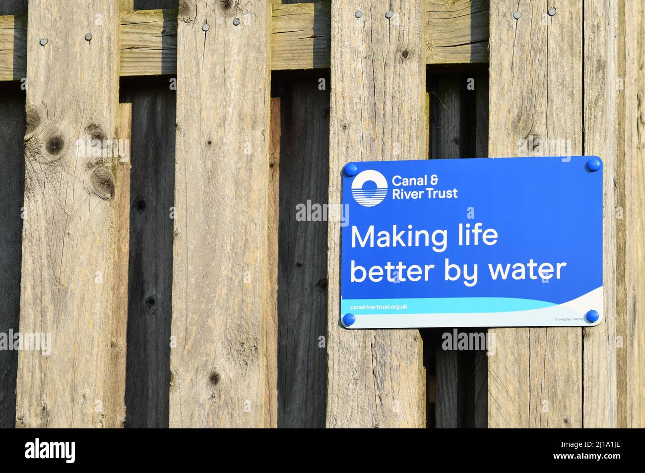 Sign: 'Canal & River Trust Making life better by water' on a wooden fence, with copy space. Stock Photo