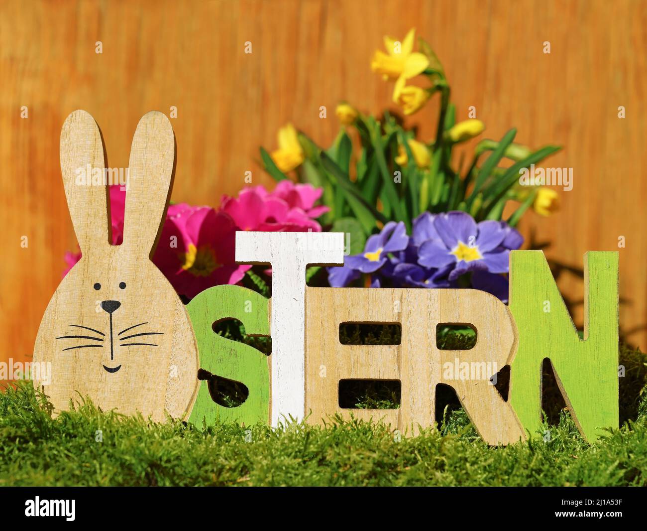 easter bunny as O in german word, ostern, written in wooden font decoraction on moss in front of colorful spring flowers Stock Photo