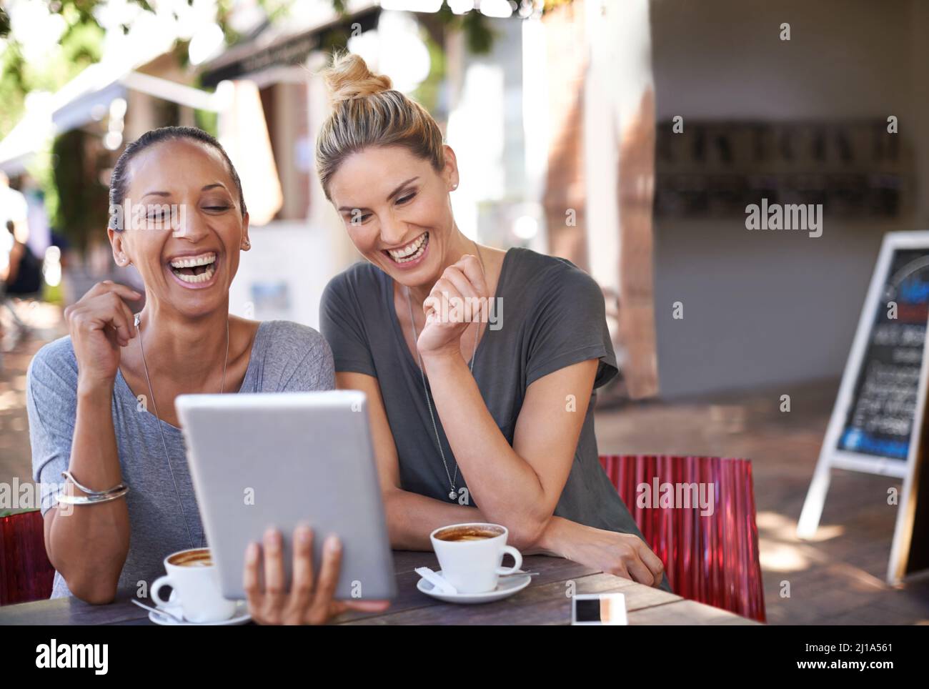 Sharing a laugh between besties. Two young women looking at a tablet in a coffee shop. Stock Photo