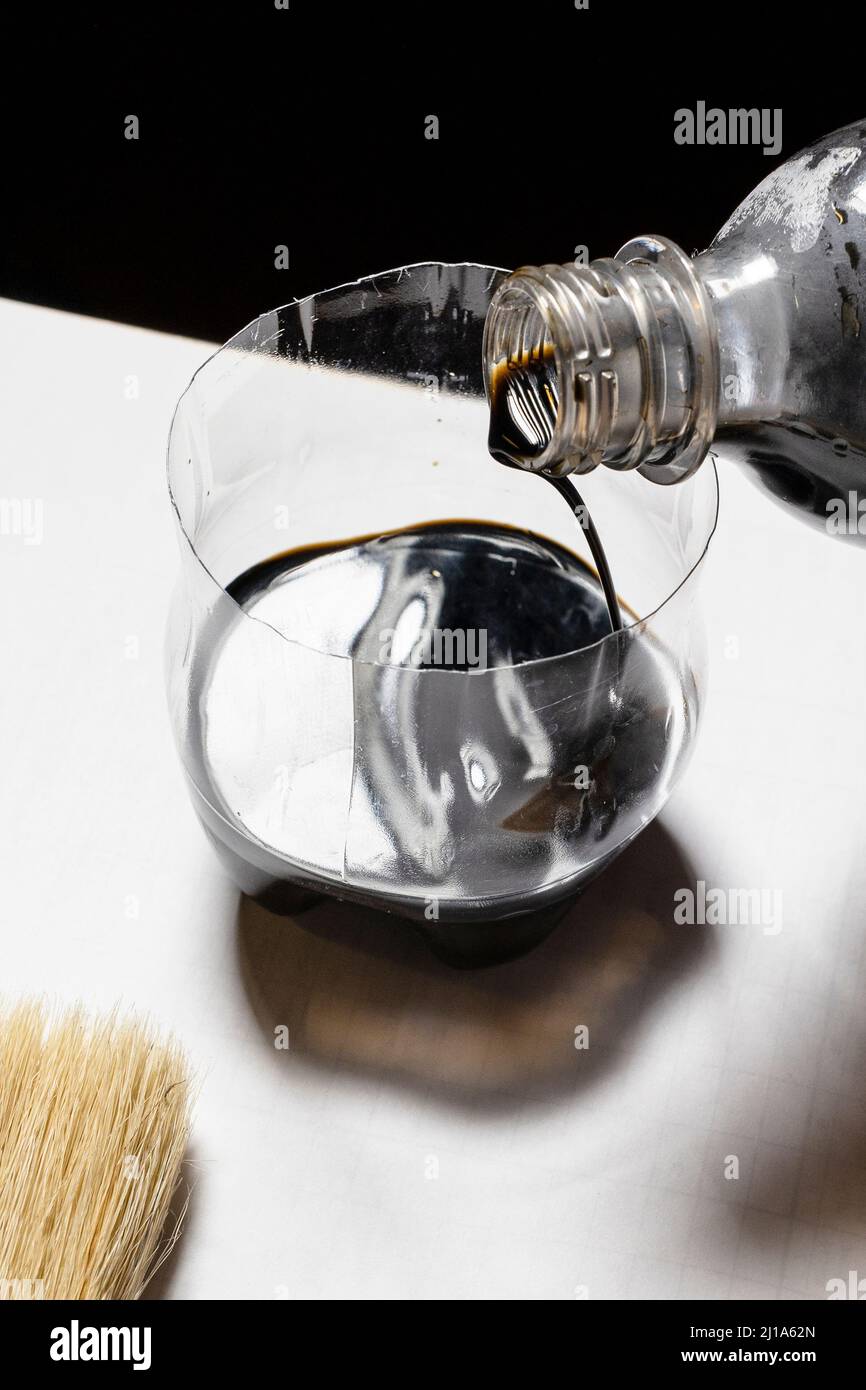 pouring wood stain from plastic bottle into jar close up at home Stock Photo