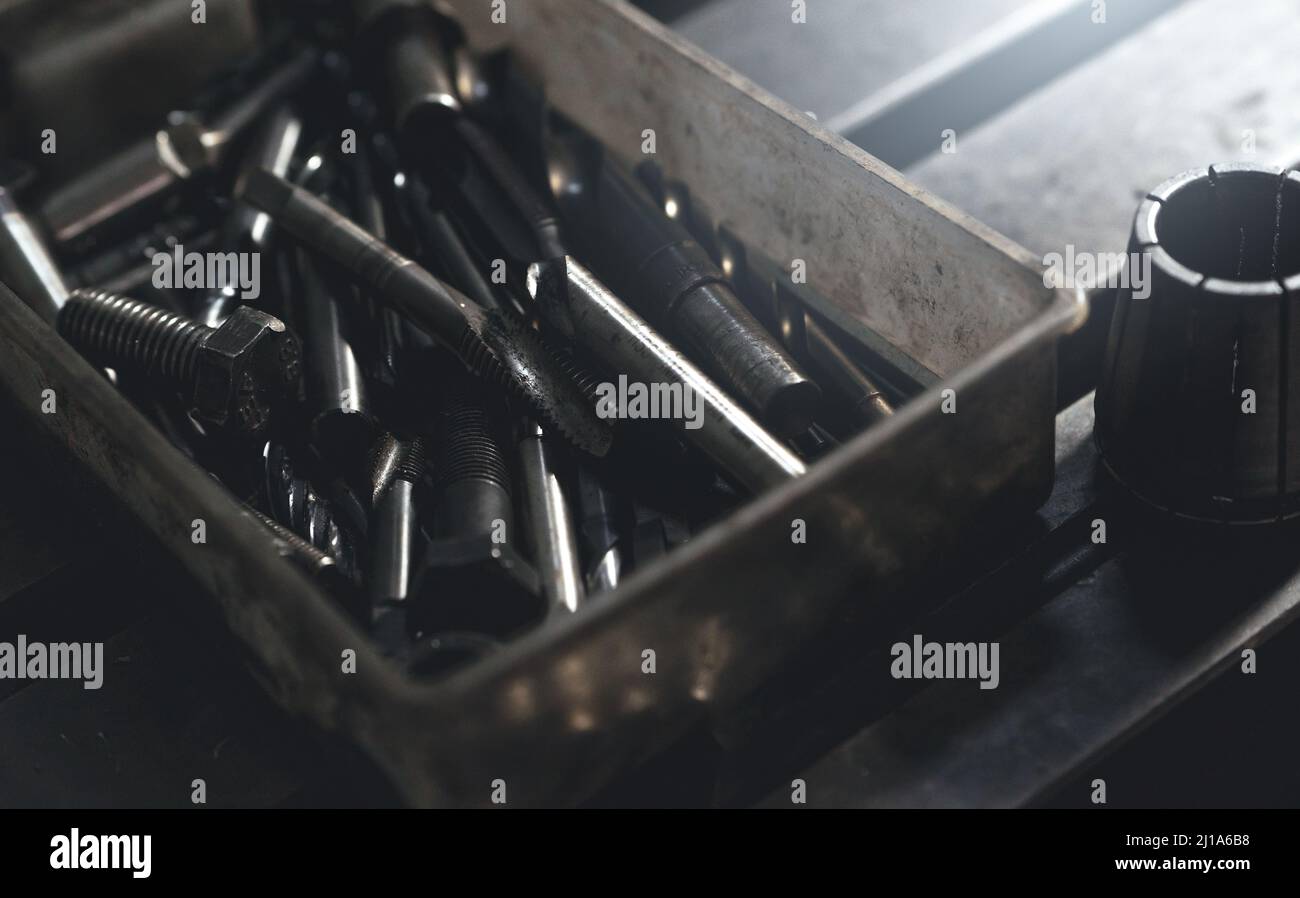 Selective focus on threaded tap, metal drill bit, and nut in old and dirty plastic toolbox. Old steel tool in box. Carbide tip metal cutter. Metalwork Stock Photo