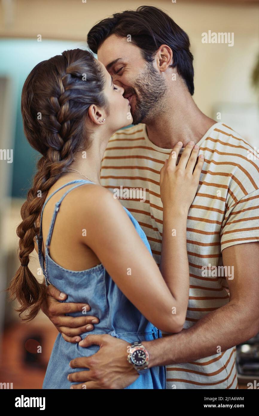 The best kisses are unexpected. Shot of an affectionate young couple kissing in their kitchen at home. Stock Photo