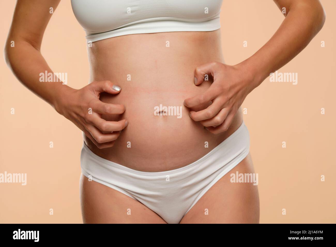 Cropped view of pregnant woman scratching  her belly isolated on beige background Stock Photo