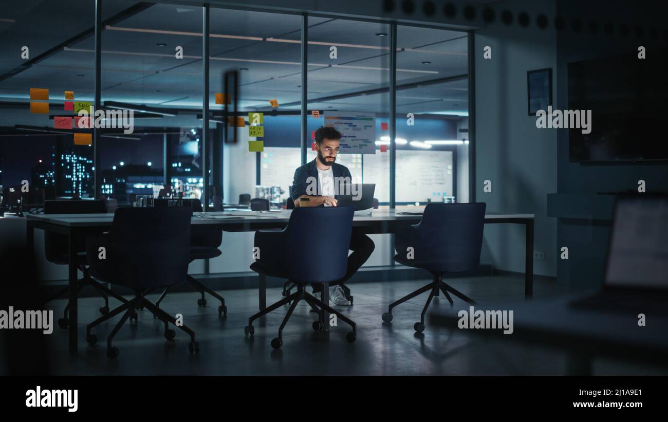 Stressed Creative Businessman Thinking; CEO Working on Laptop Computer in Big City Office Late in the Evening. Businessman Preparing for a Meeting Dis Stock Photo