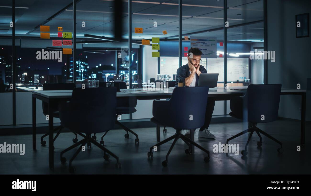 Successful Handsome Creative Director Working on Laptop Computer in Big City Office Late in the Evening. Businessman Preparing for a Marketing Plan Me Stock Photo