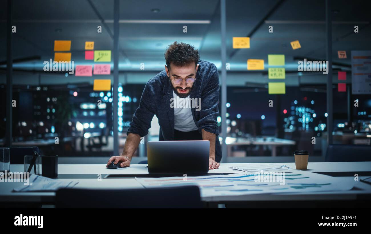 Successful Handsome Creative Director Working on Laptop Computer in Big City Office Late in the Evening. Businessman Preparing for a Marketing Plan in Stock Photo
