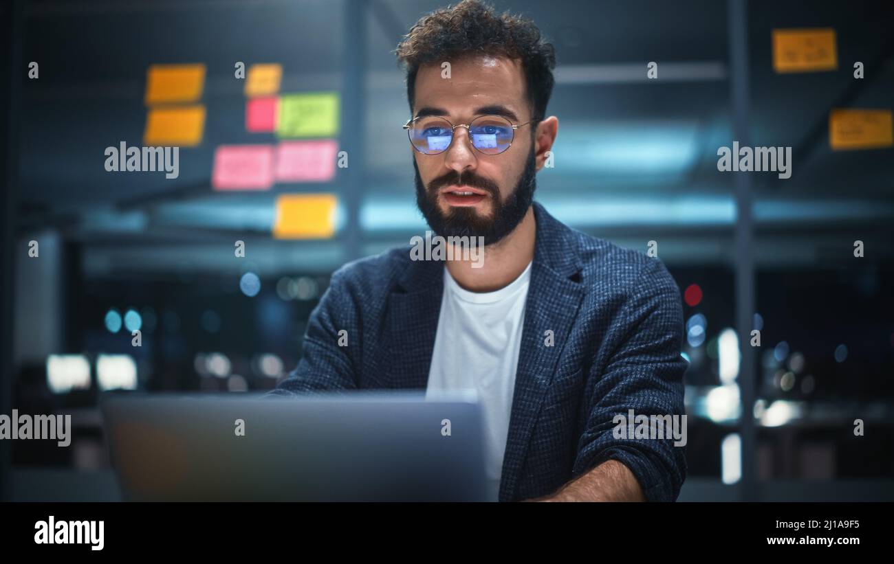 Successful Handsome Creative Director Working on Laptop Computer in Big City Office Late in the Evening. Businessman Preparing for a Marketing Plan in Stock Photo