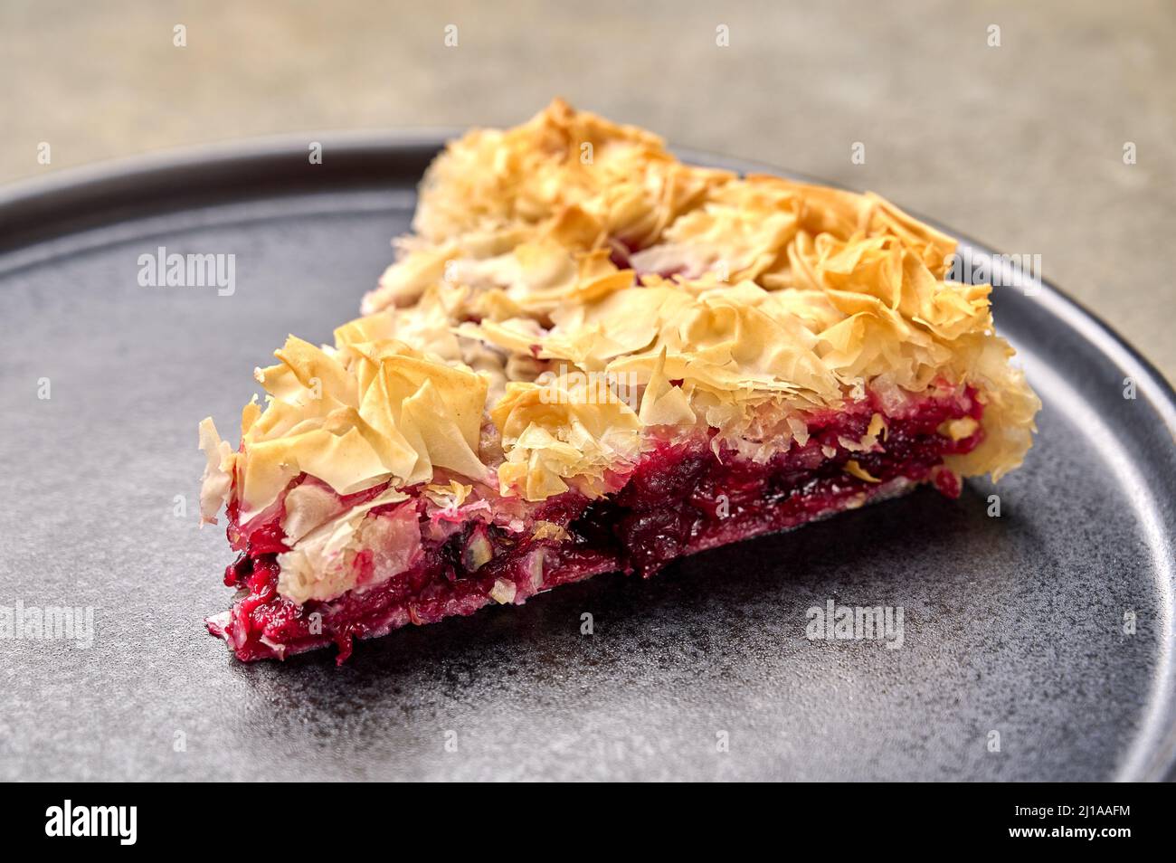 Piece of homemade cherry pie from filo dough on dark plate. Selective focus, close up Stock Photo