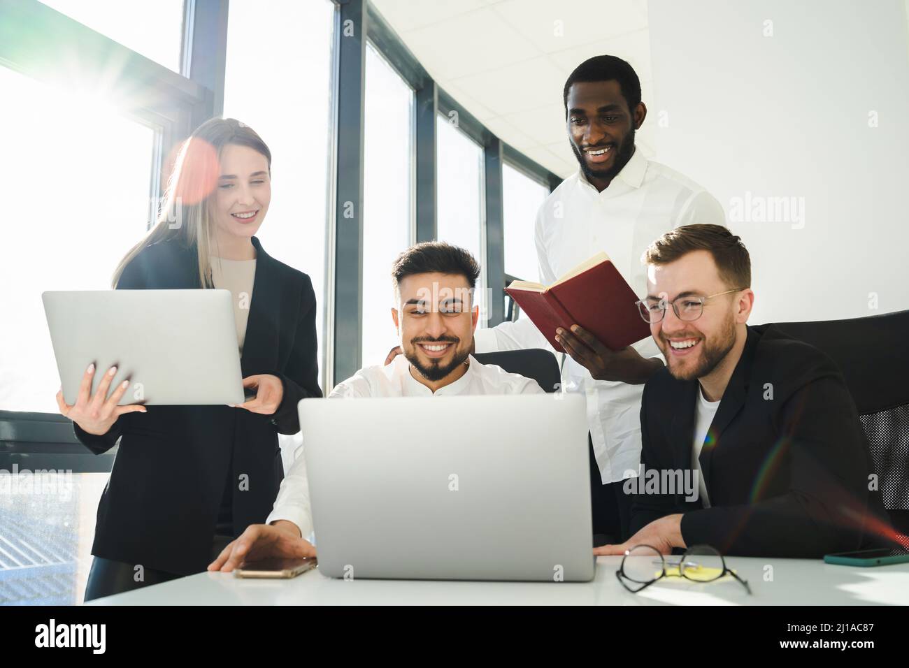 Group of multiracial office workers laughing while looking at laptop.  Employees of the company are working on a new project Stock Photo