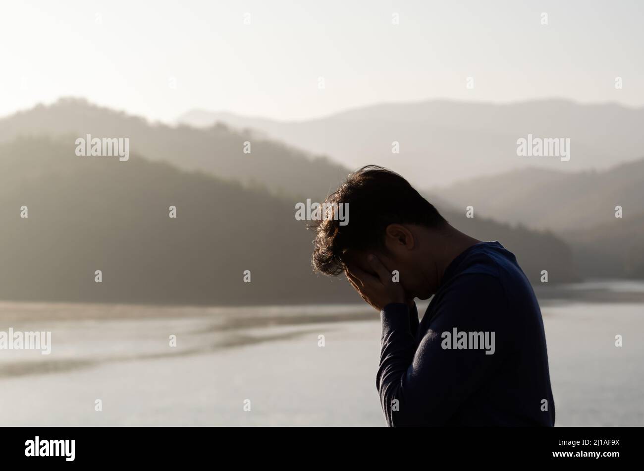 Asian miserable depressed man stand alone with mountain and lake background. Depression and mental health concept. Stock Photo