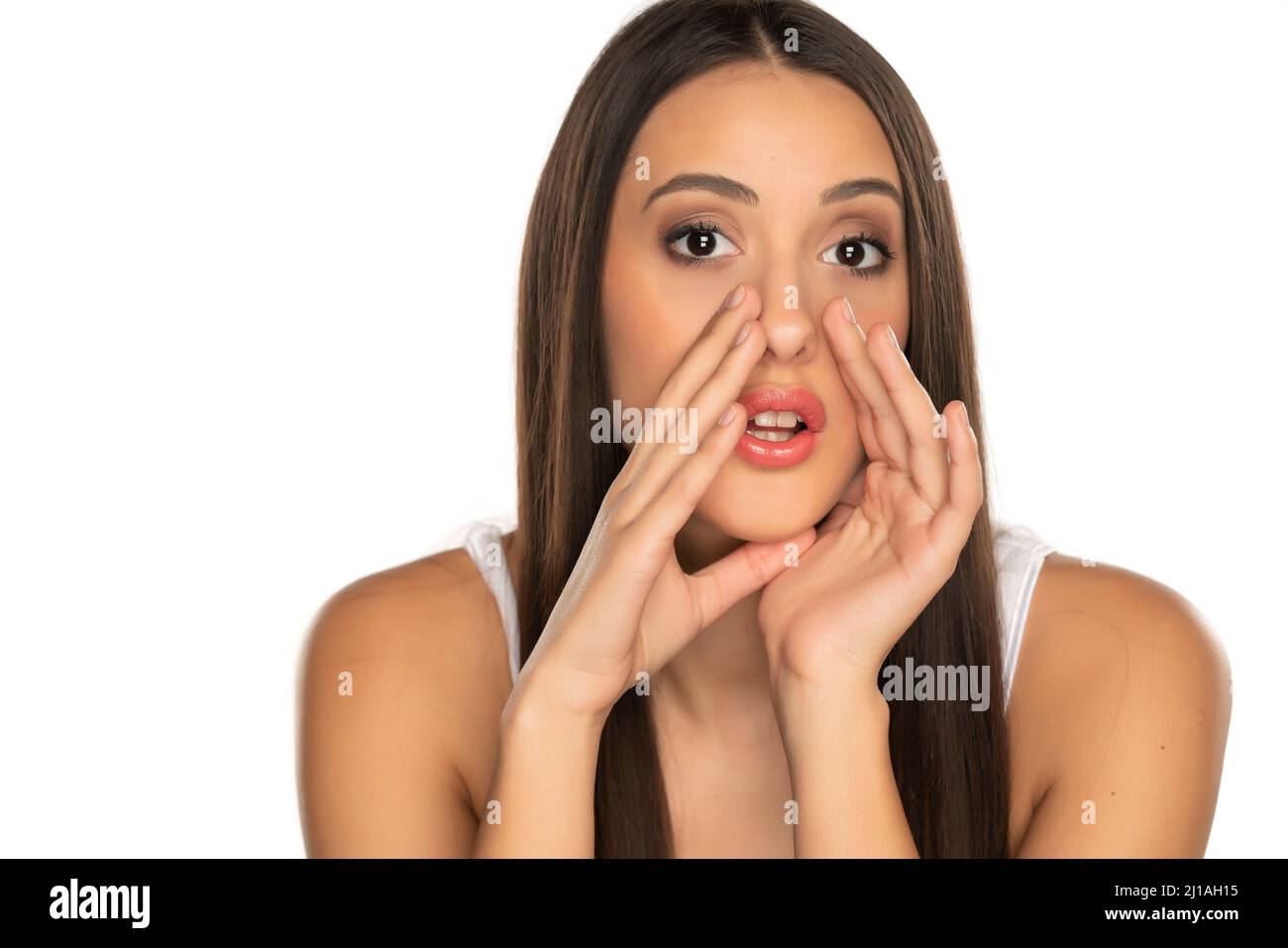 Young woman is holding hands near mouth and telling a secret on a white background Stock Photo
