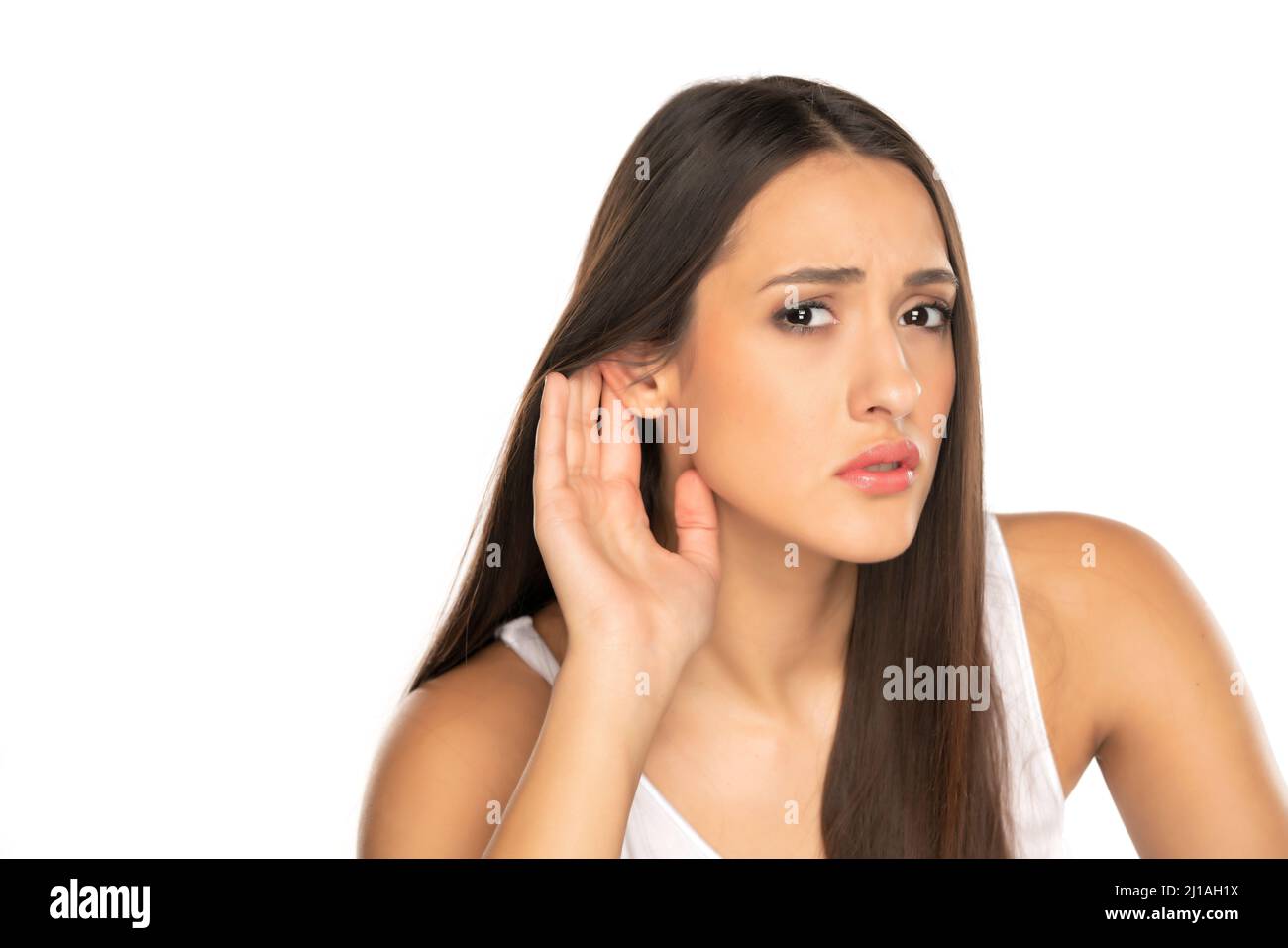 Young woman over isolated white background listening to something by putting hand on the ear Stock Photo