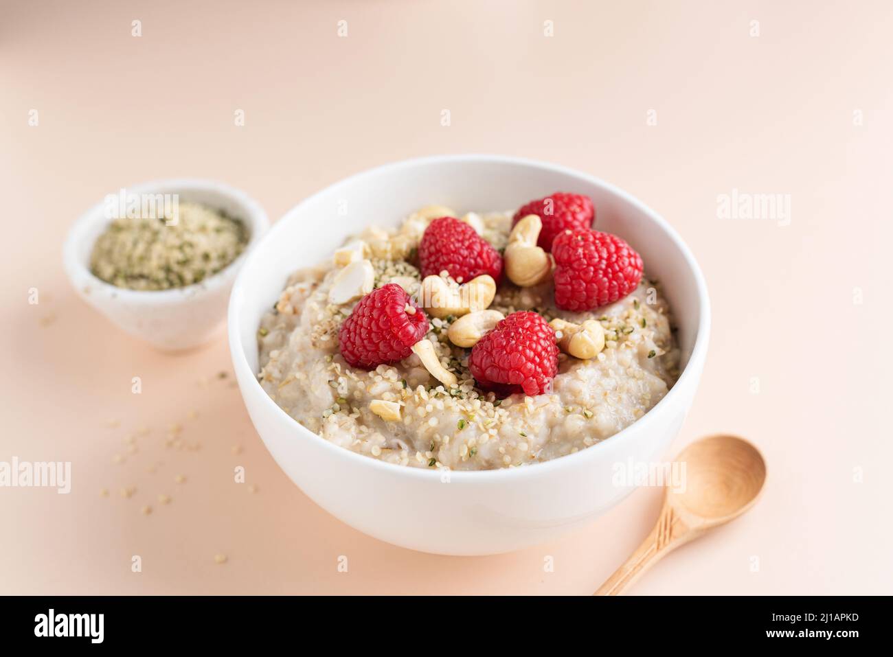 Oatmeal porridge with rasbperries, hemp seeds and cashews on beige background. Healthy breakfast food for dieting, weight loss Stock Photo