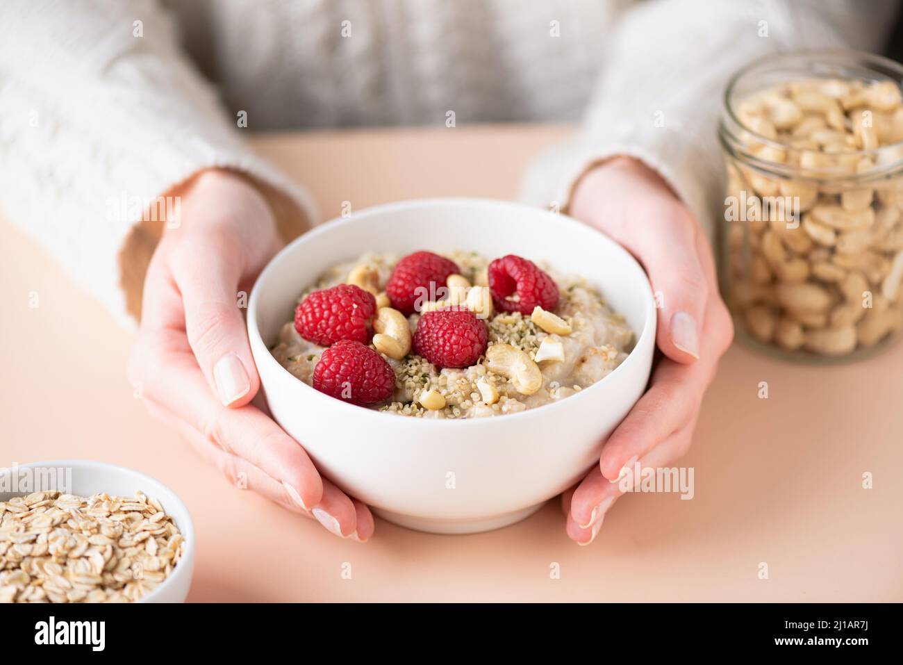 Oatmeal porridge with berries and seeds in caucasian female hands. Concept of eating healthy, vegan lifestyle, dieting Stock Photo