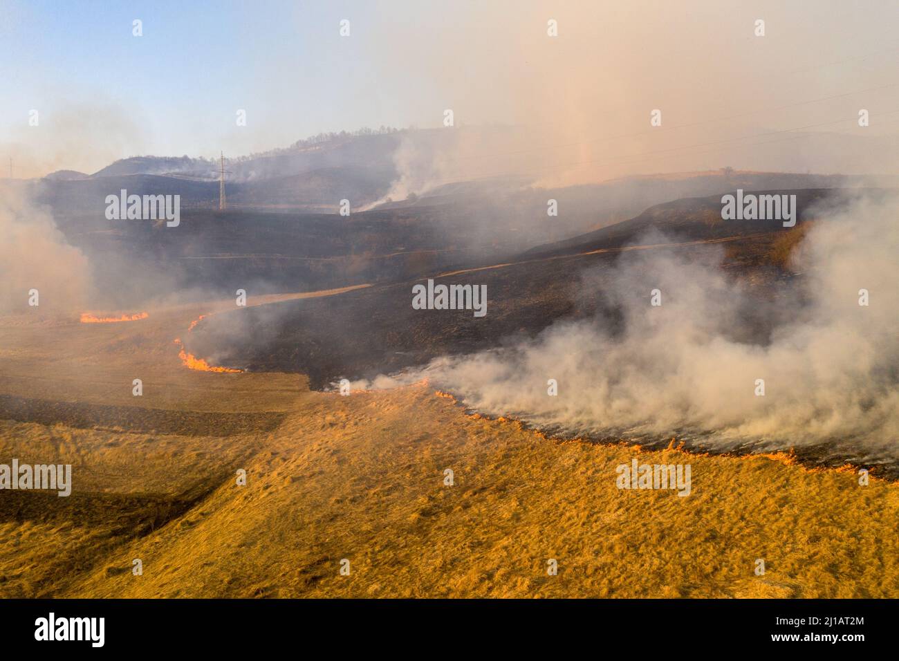 Aerial view of spring dry grass burning field. Fire and smoke in the meadow, nature pollution and danger, shrubs and common waste are burned in Romani Stock Photo