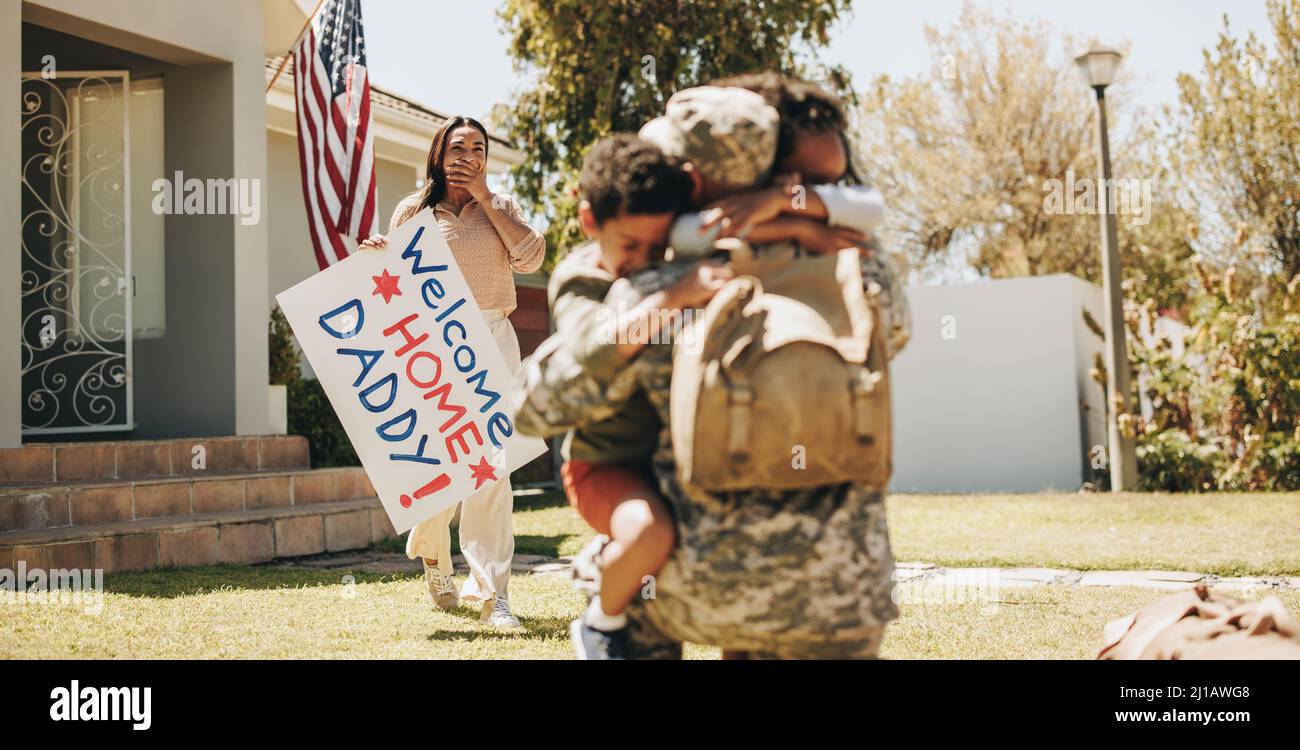 Patriotic soldier being welcomed by his family at home. American serviceman embracing his children after returning home from the army. Military man re Stock Photo