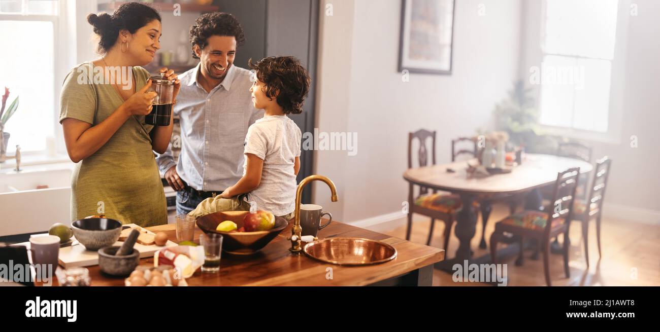 Ethnic parents spending some quality time with their son in the kitchen. Mom and dad smiling while talking to their son at breakfast time. Happy young Stock Photo
