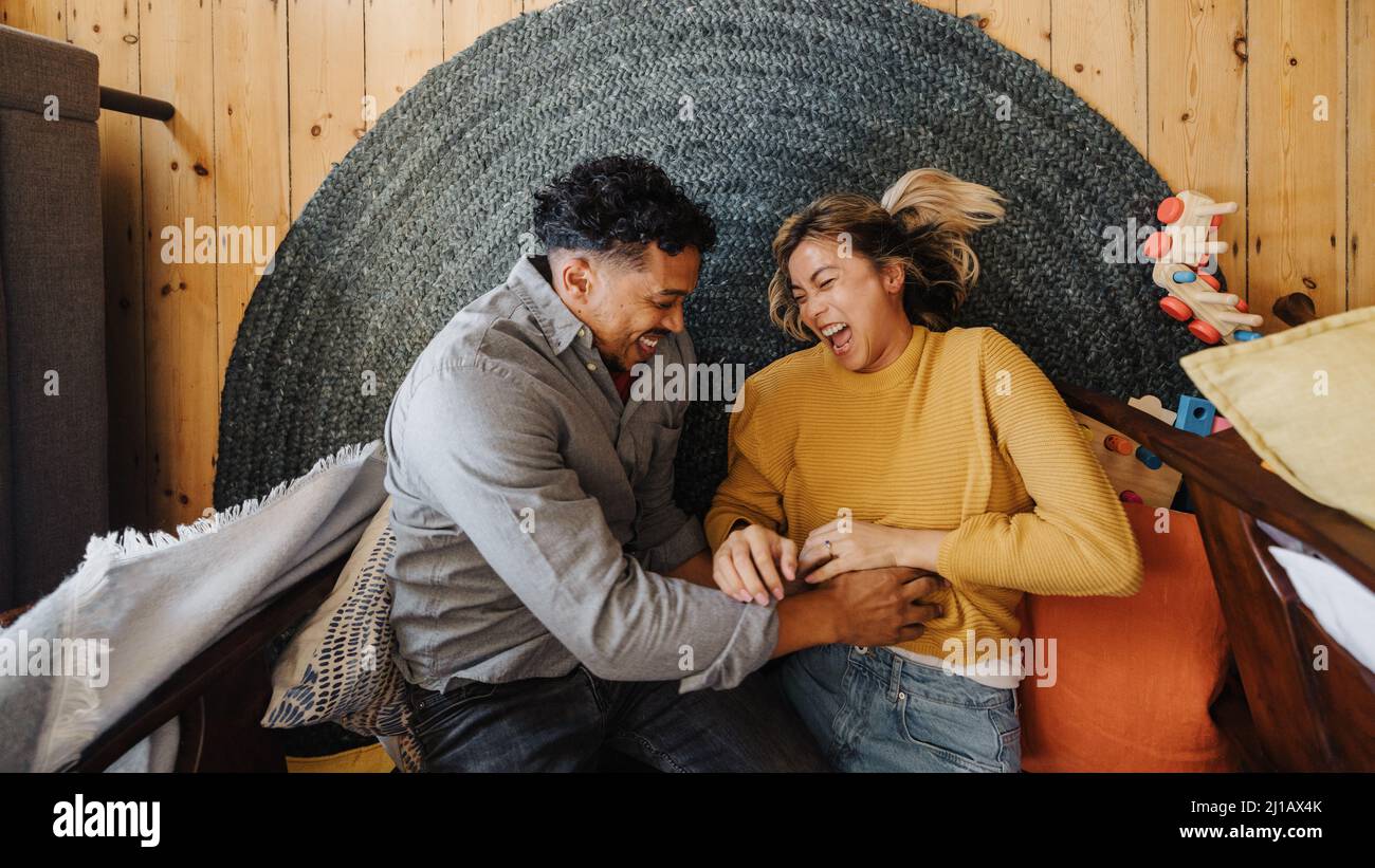 Overhead view of a married couple laughing together while lying in their children's play area. Two happy young parents having fun with each other. Cou Stock Photo