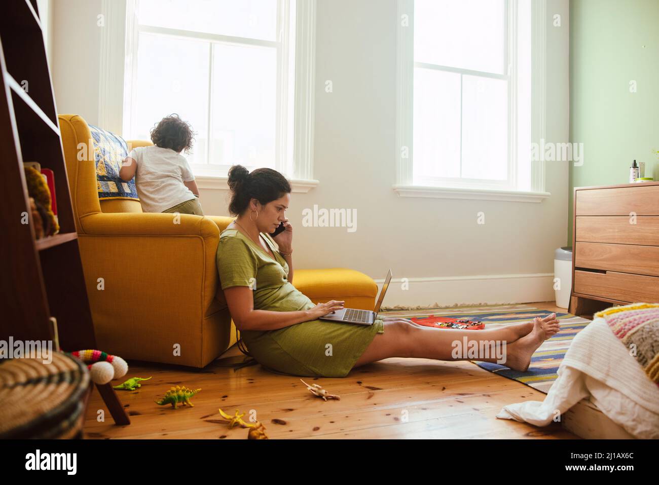 Mom working from home during quarantine. Working mom speaking on the phone while sitting in her son's play area. Single mother communicating with her Stock Photo