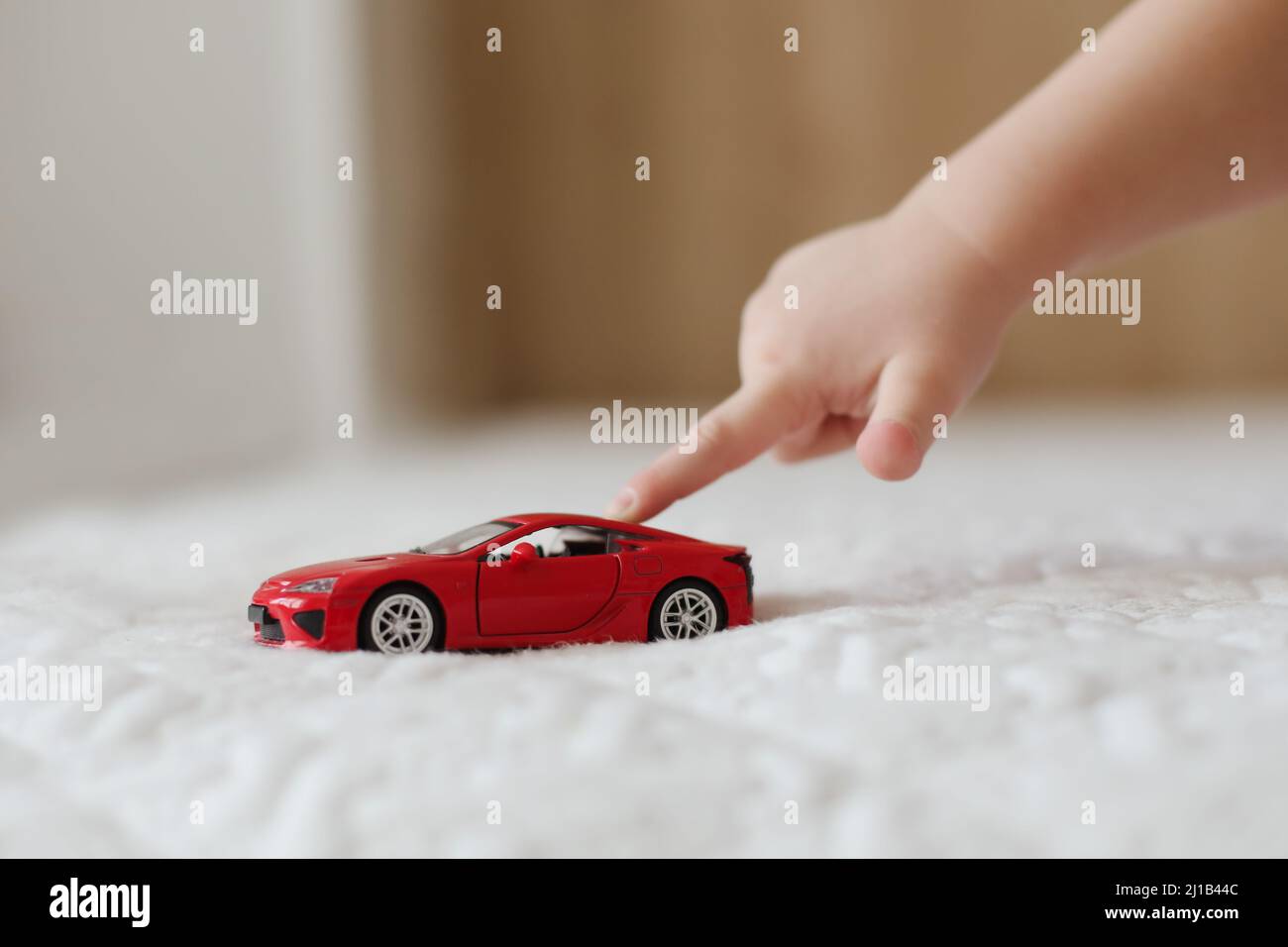 close-up of child hand playing with toy car. hand of a little kid pushing a plastic toy car on the white background Stock Photo