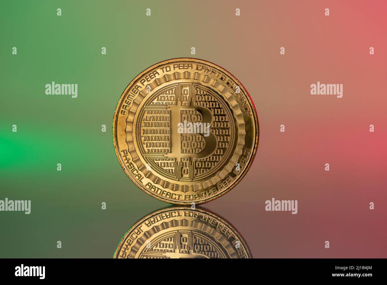 Bitcoin BTC cryptocurrency physical coin placed on the reflective surface and lit with green and red lights. Stock Photo
