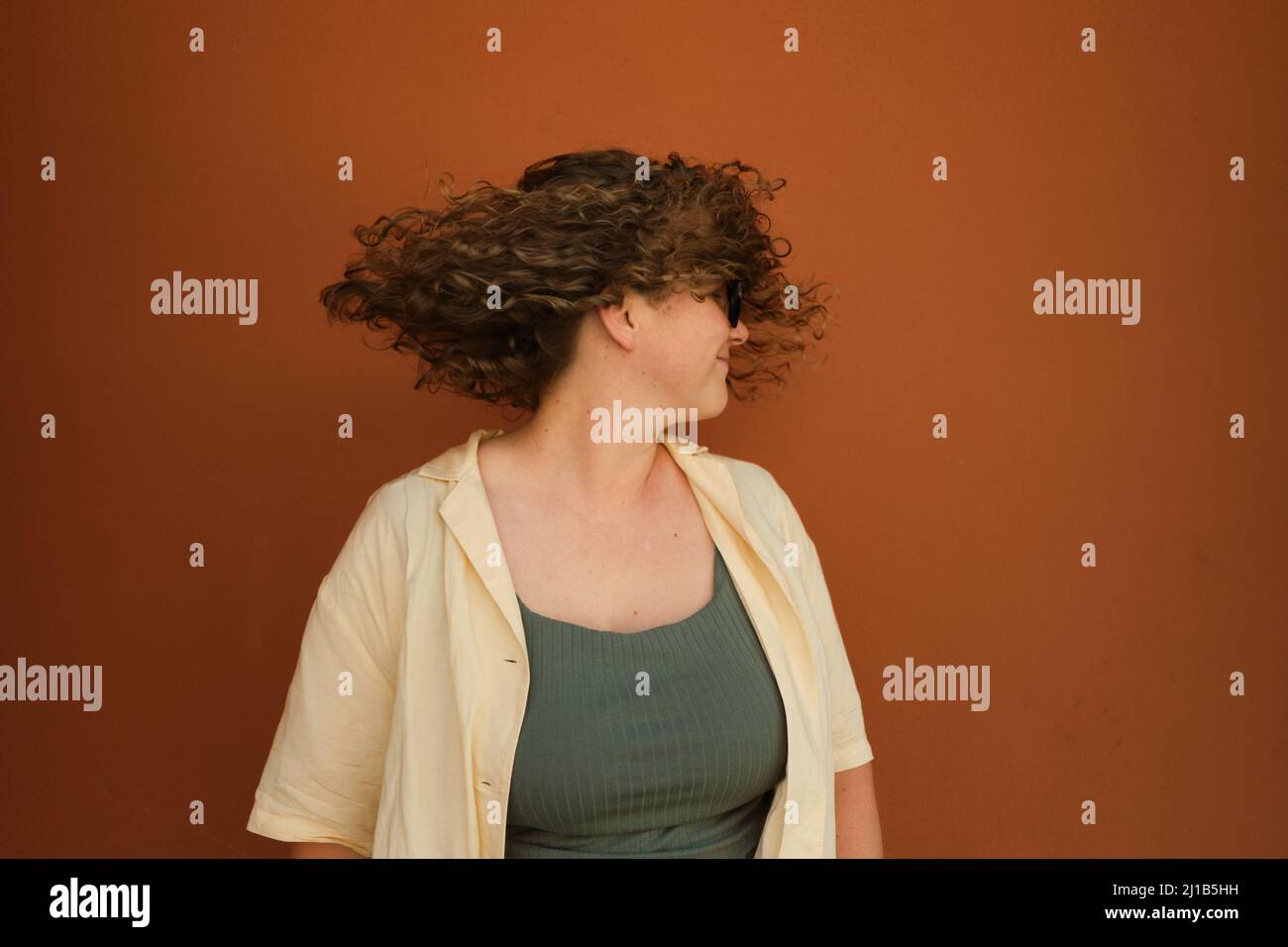 Happy caucasian white girl on orange background shakes her head. Curly hair flies to sides. Hair care. Happyness Stock Photo