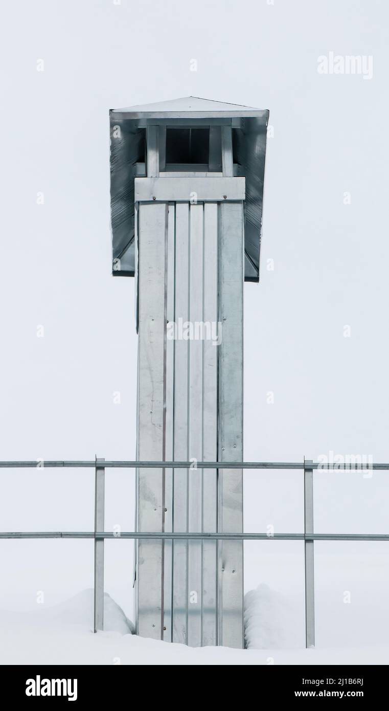 Rectangular metal chimney on the roof of the house. There is white snow on the surface. Against the background of a gray sky. Cloudy winter day, soft light. Stock Photo