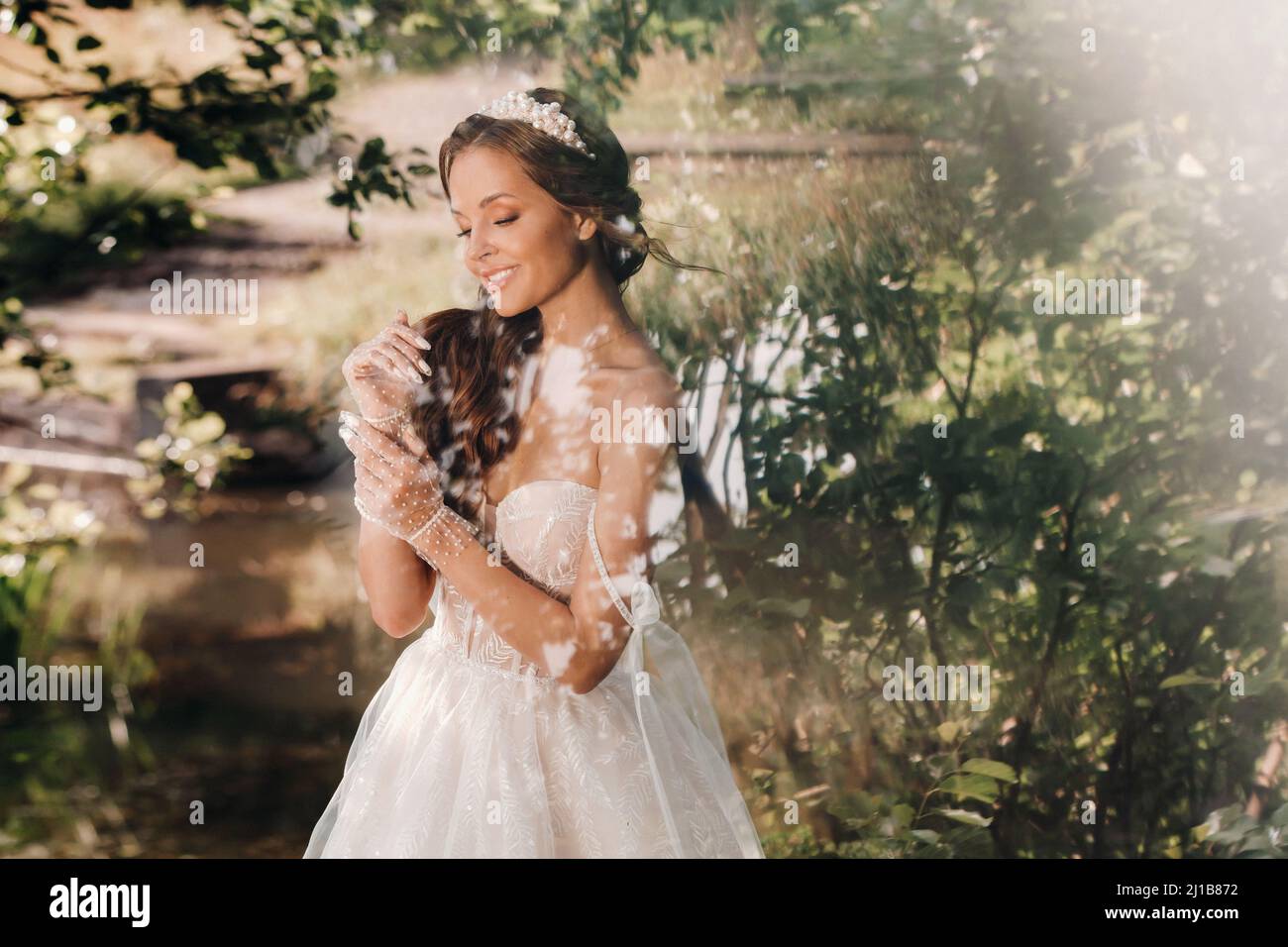 An elegant bride in a white dress, gloves with a bouquet on a waterfall ...