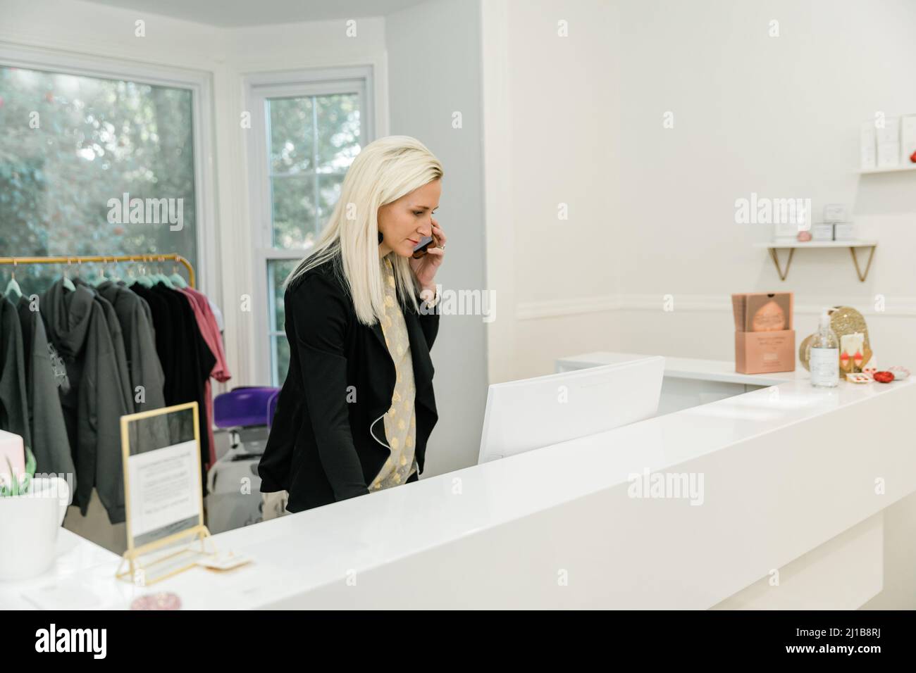 A female small business owner of a medical spa and retail shop standing behind the counter with a computer working Stock Photo