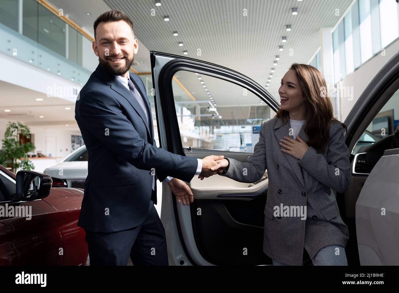 an employee of a car dealership helps a young woman with a choice of a