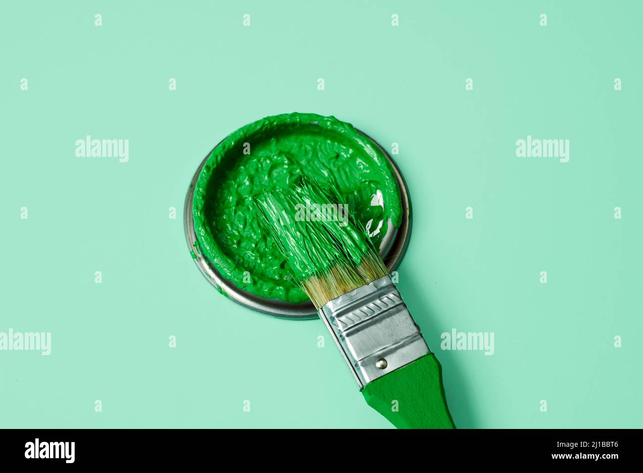 closeup of a paintbrush and the lid of a paint can with green pain, on a pale green background Stock Photo