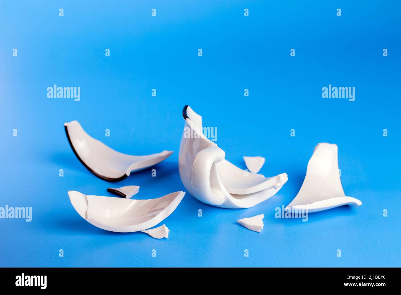 Broken white cup on  blue background. Concept disintegration, mockup Stock Photo