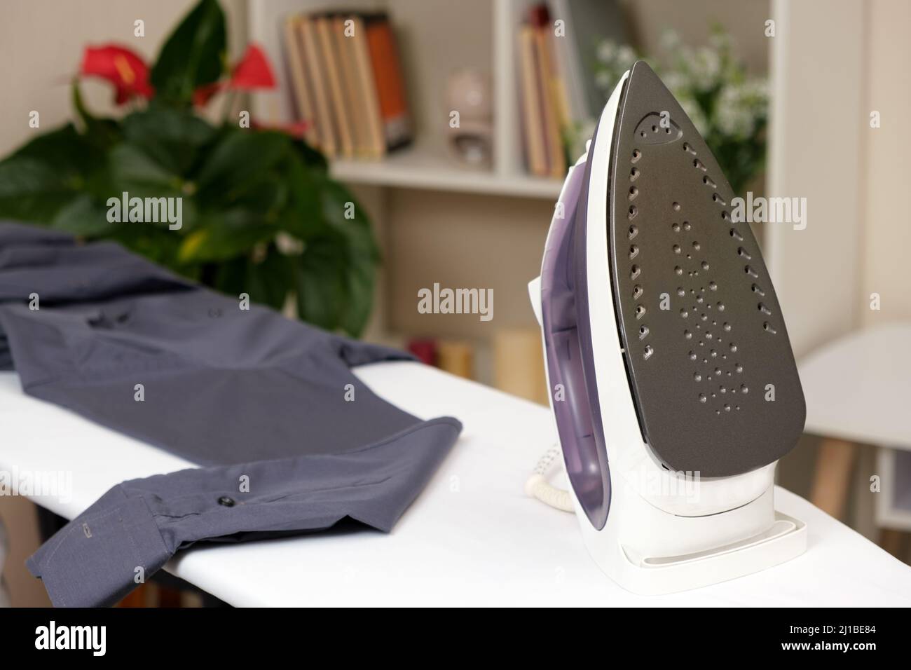 Iron on a white ironing board and a gray men's shirt. Care of clothes