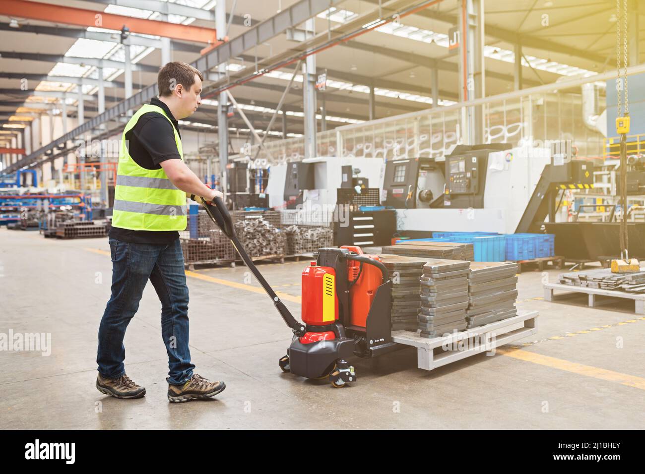 Warehouse worker dragging hand pallet truck or manual forklift with the