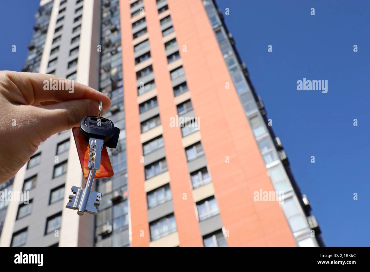House keys in male hand on background of new tower building. Real estate agent, moving home or renting property Stock Photo