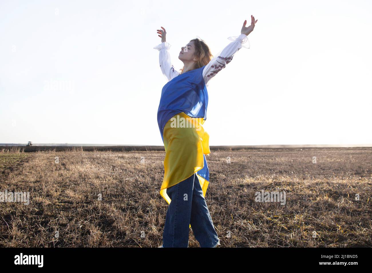 young woman is wrapped in yellow and blue Ukrainian flag. request for help to Ukraine, drawing attention to issue of supporting Ukrainians. independen Stock Photo