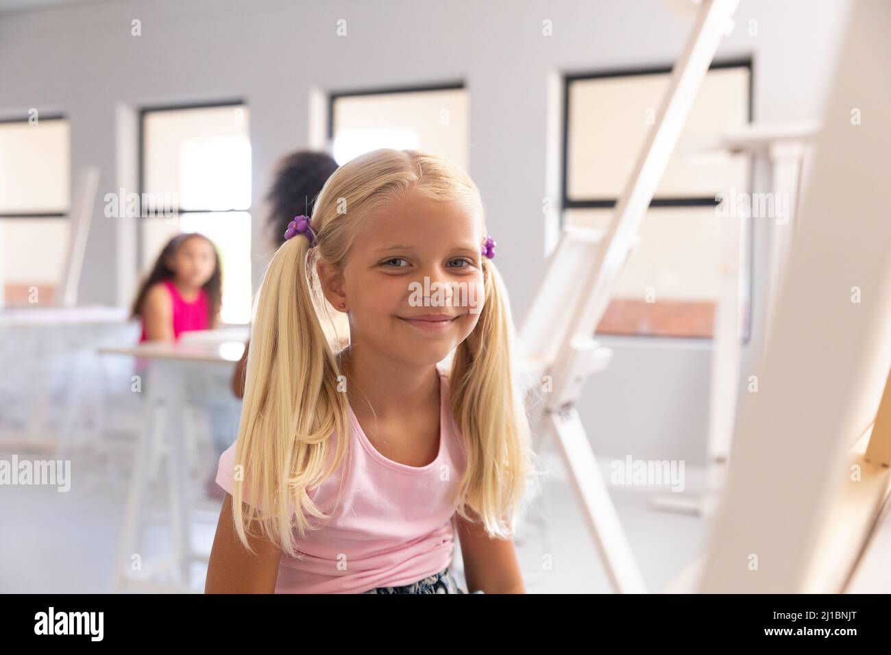 Portrait of smiling caucasian elementary schoolgirl sitting on chair by ...