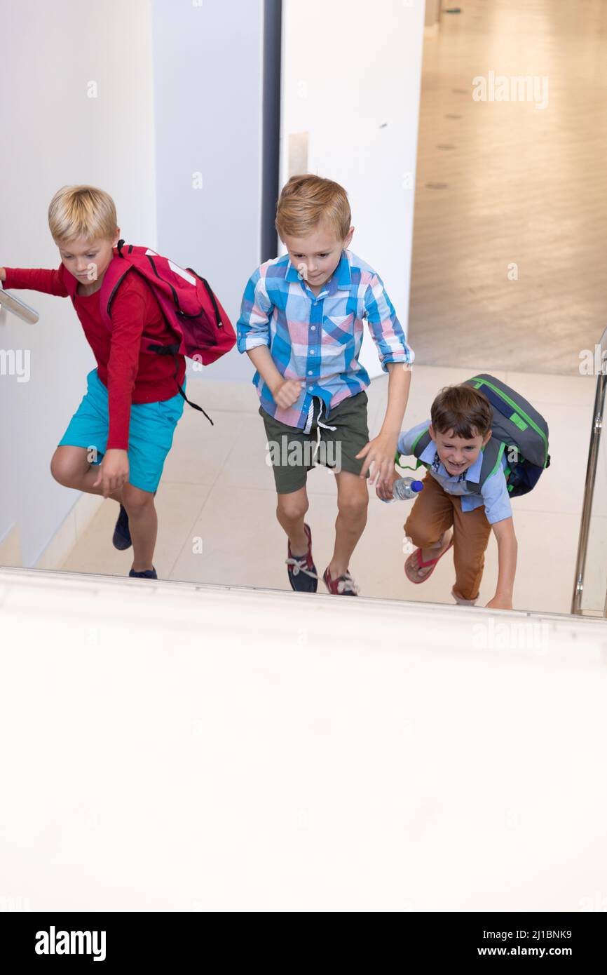 Caucasian elementary schoolboys with backpack climbing on steps in school building Stock Photo