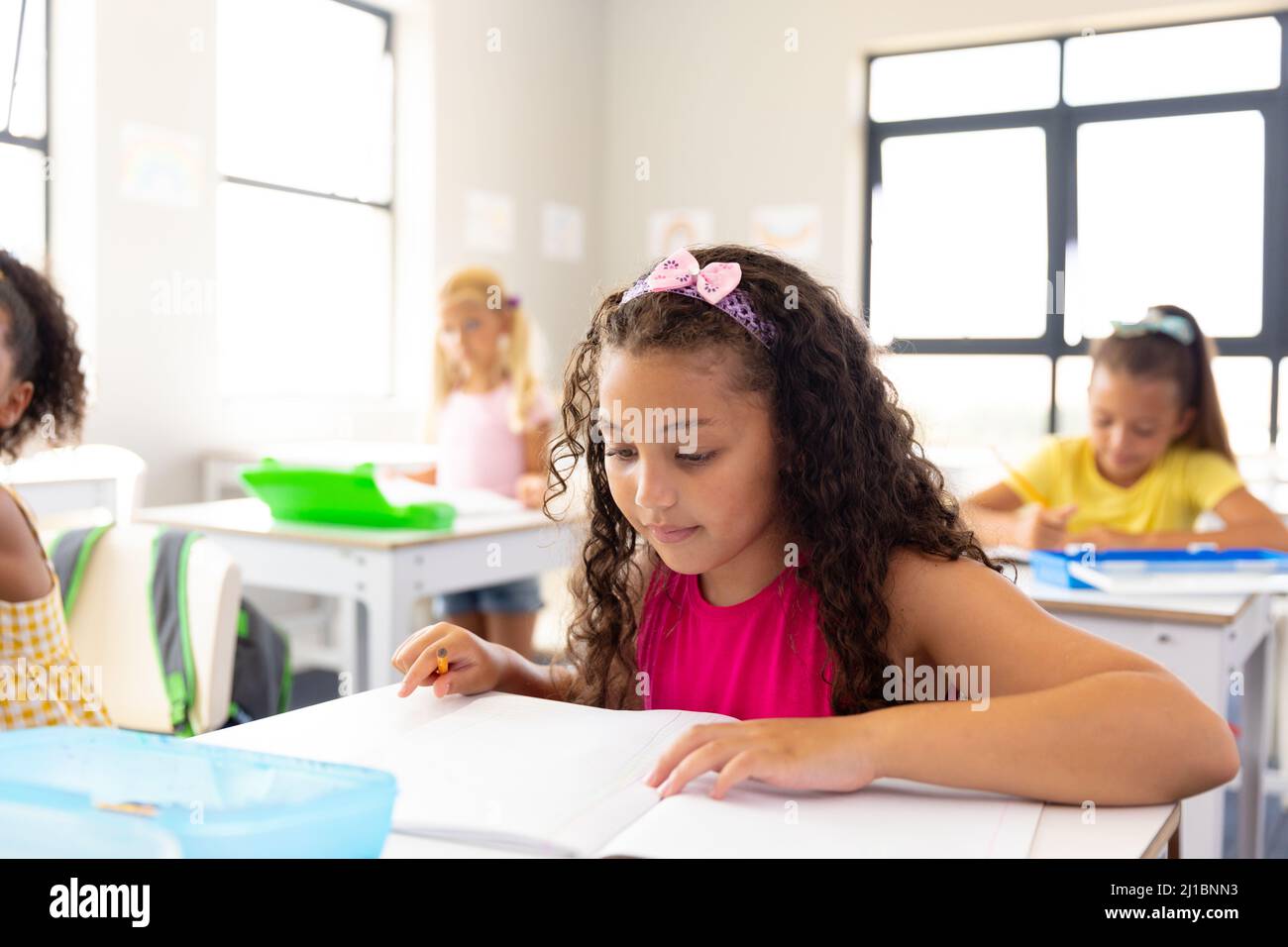 Multiracial elementary schoolgirls studying at desk in classroom Stock ...